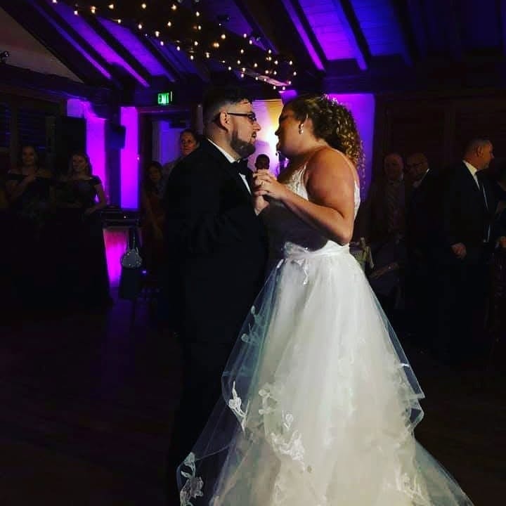 Couple sharing first dance at wedding reception with purple uplighting