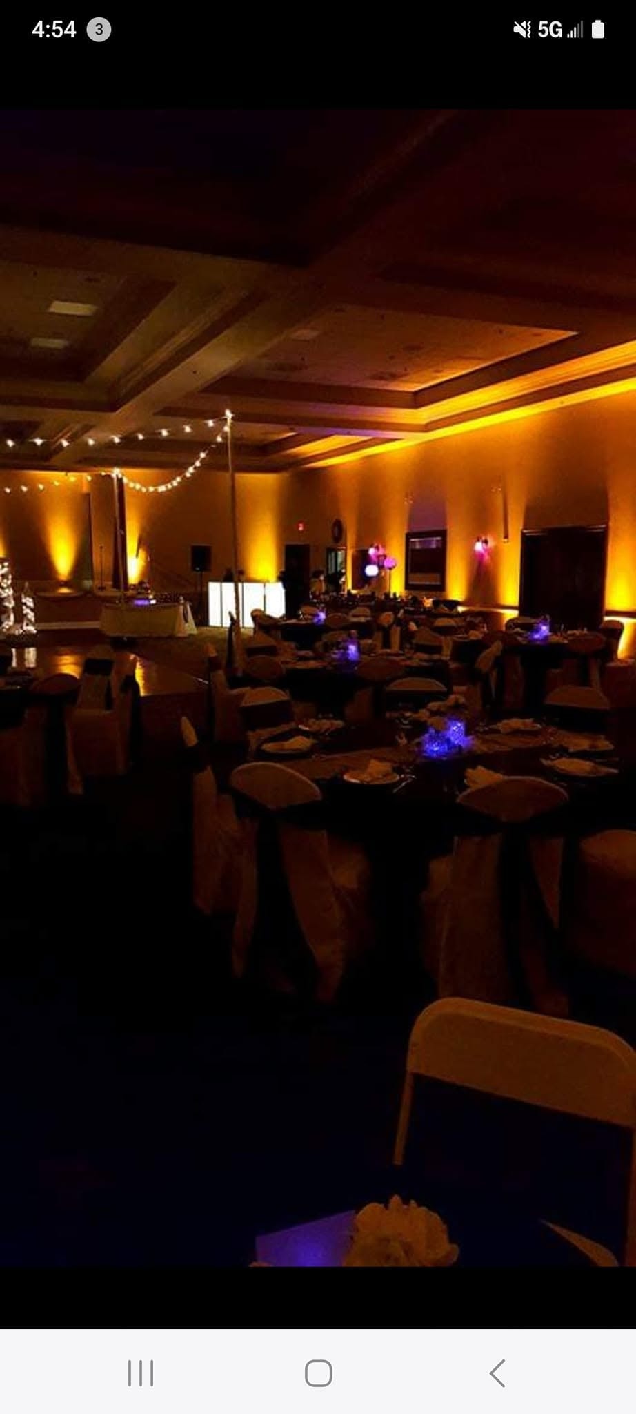 Elegant ballroom with warm gold LED uplighting and string lights